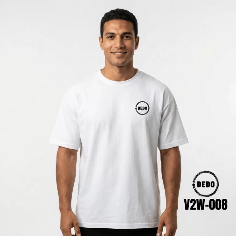 Rear view of a smiling man looking over his shoulder on a sunny waterfront promenade with feluccas in the background, wearing a white oversized t-shirt with a highly detailed, black cybernetic skull graphic print on the back integrated with circuit board wiring and mechanical details. The DEDO logo and product code V2W-008 are visible in the lower corner.