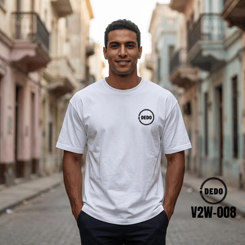 Rear view of a smiling man looking over his shoulder on a sunny waterfront promenade with feluccas in the background, wearing a white oversized t-shirt with a highly detailed, black cybernetic skull graphic print on the back integrated with circuit board wiring and mechanical details. The DEDO logo and product code V2W-008 are visible in the lower corner.